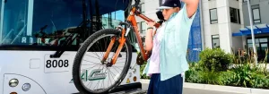 A Young Boy Placing His Orange Bike Onto An Ac Transit Bus