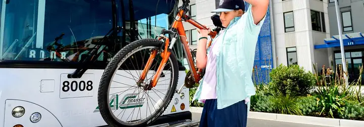 A Young Boy Placing His Orange Bike Onto An Ac Transit Bus